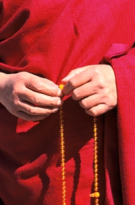 The Dalai Lama's holding mala beads in his hands.